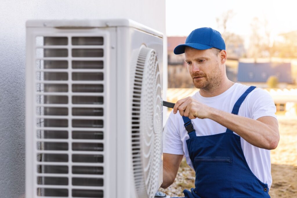 A picture of an HVAC service technician with tools working on an outdoor white HVAC unit