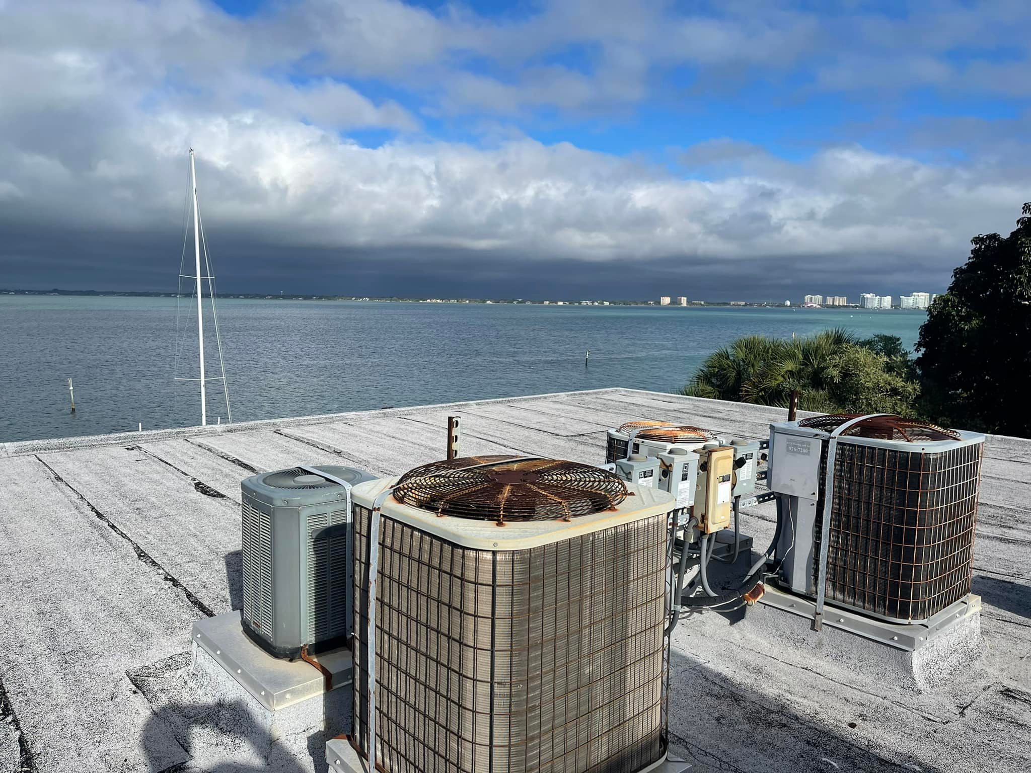 A picture of an air conditoiner unit with a cloudy sky amidst a backdrop of water in the background